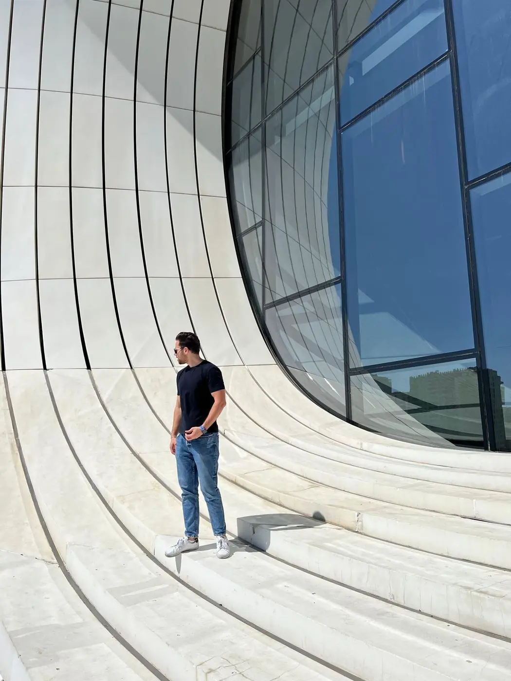Ahmad Tello standing on white curved stone steps beside a glass facade